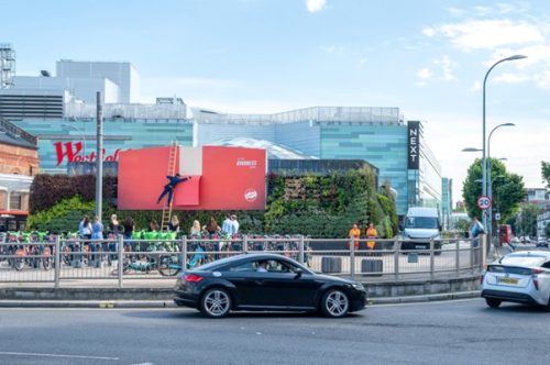 Najciekawsze reklamy zewnętrzne – przykłady i kreatywne kampanie, które musisz znać 4 Zdjęcie przedstawiające przykład reklamy zewnętrznej - Babybel - Billboard "Peel and Reveal" w miejskim krajobrazie.